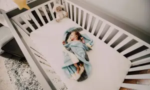 Nowe życie otulone w miękką pościel dla dzieci. Maleństwo śpi spokojnie w łóżeczku, obok pluszowa owieczka.