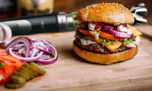 Pyszny hamburger z serem, warzywami i domowym sosem do hamburgerów. Obok pokrojona cebula i ogórki.