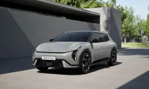 Nowy Kia EV4 GT-Line w kolorze srebrnym, zaparkowany przed nowoczesnym budynkiem z zielenią w tle.