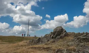 Wanderer auf dem Herzogenhorn genießen die Aussicht unter dramatischen Wolken. Ein Holzkreuz markiert den Gipfel.