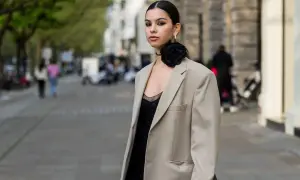 Eine Frau mit schwarzer Blume am Hals trägt ein beiges Sakko über einem schwarzen Kleid. So lässt sich ein festliches Kleid mit Jacke kombinieren.