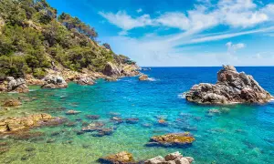 Piękna pogoda w Lloret de Mar w czerwcu. Turkusowa woda, skaliste wybrzeże porośnięte zielenią, błękitne niebo z chmurkami.