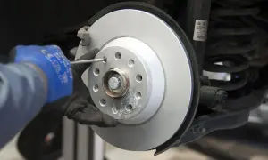 Mechanik w niebieskiej rękawicy dokręca śrubę nowej tarczy hamulcowej. Wymiana tarcz hamulcowych w toku.