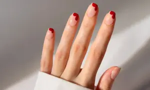 Une main aux ongles nude ornés de petits cœurs rouges. Une idée ongle coeur parfaite pour la Saint-Valentin ou pour ajouter une touche d'amour à votre quotidien.