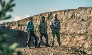 Trzech mężczyzn w spodniach skiturowych męskich i kurtkach na tle skalnego krajobrazu.