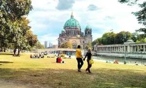 Ett par promenerar på en gräsmatta med Berlin domkyrka i bakgrunden. Många njuter av solskenet, en perfekt dag för aktiviteter i Berlin.