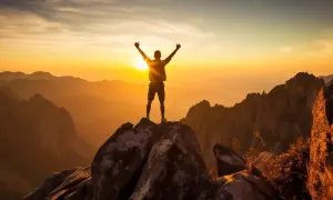Hombre en la cima de una montaña al amanecer, celebrando su **crecimiento personal y espiritual**.