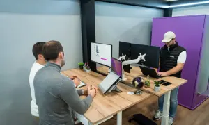 Trois personnes travaillent dans un bureau flex office moderne. L'un est debout devant un écran, les deux autres sont assis à un bureau.