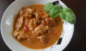 Pyszny gulasz wieprzowy w sosie z papryką i bazylią, podany w białej misce.