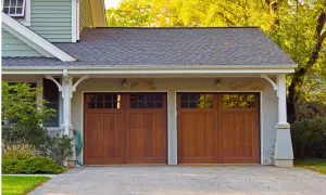 Doppio garage con porte in legno scuro, un box di pertinenza si può vendere separatamente. Alberi autunnali sullo sfondo.