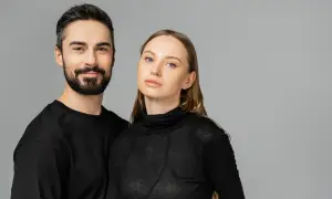 Para, która uosabia styl unisex. Mężczyzna z zarostem i kobieta o delikatnych rysach, oboje w czarnych, prostych ubraniach.