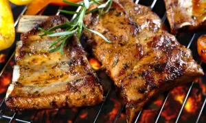 Soczyste żeberka z grilla, przyprawione ziołami, pieczone na żarze. Obok grillowana papryka i pomidory.