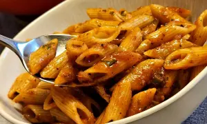 Eine Löffelportion Penne all'Arrabiata, mit einer würzigen Tomatensauce und Kräutern, wird aus einer Schüssel gehoben.