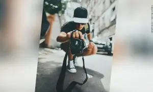 Młody fotograf w czapce z daszkiem trzyma aparat, gotowy do uchwycenia chwili. Zastanawiasz się, ile zarabia fotograf?