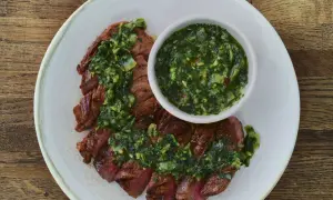 Pokrojony stek z wołowiny polany zielonym sosem chimichurri, podany na talerzu.