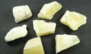 Kilka surowych bryłek kalcytu miodowego o delikatnym, żółtawym odcieniu, ułożonych na ciemnym tle.