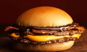 Gros plan sur un burger double viande, fromage fondant, bacon croustillant et sauce barbecue, sur une planche en bois.