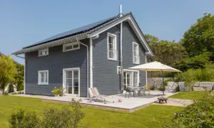 Dunkelgraue Hausfassade mit weißen Fenstern und Türen. Beispiele für Hausfassade Farbe: Dieses moderne Haus mit Solaranlage und Terrasse lädt zum Entspannen ein.
