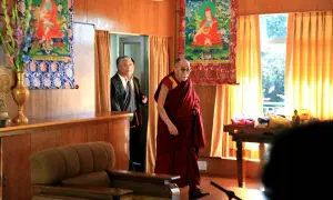 Dalai Lama i sin klädsel, med en man i kostym bakom. En inblick i var bor Dalai Lama, med buddhistisk konst på väggarna.