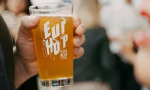 Un bicchiere di birra dorata con il logo "Eur Hop Roma Beer Festival" tenuto in mano.