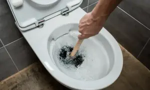 Hand plunges a toilet that is verstopft immer wieder. Water splashes around the plunger.