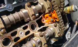 Detalle de un motor con el árbol de levas y el cigüeñal expuestos, junto a una cadena de distribución naranja.