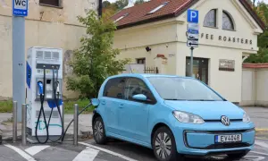 Niebieski Volkswagen Up ładuje się przy stacji ładowania. Obok znajduje się budynek z napisem "COFFEE ROASTERS".