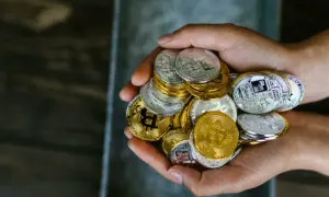 Mani che stringono una manciata di monete d'oro e d'argento, simboleggiando i criptovalute rischi e vantaggi.