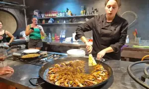 Kobieta w czarnym fartuchu przygotowuje na kuchence ogromną patelnię z owocami morza i ryżem. To musi być najlepsza paella w Barcelonie!