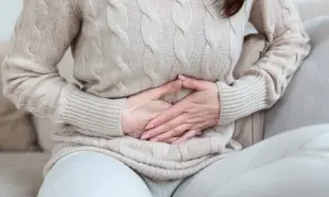 Kobieta w beżowym swetrze trzyma się za brzuch, odczuwając bolesne rozpychanie dziecka w brzuchu.