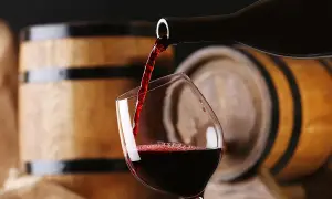 Versando un ricco aglianico vino in un bicchiere, con botti di legno sullo sfondo.