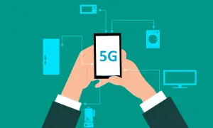 Dłonie trzymają smartfon z napisem 5G, połączony z różnymi urządzeniami domowymi. To pokazuje, co to jest 5G – przyszłość łączności.
