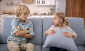Bambini che litigano sul divano. Lui incrocia le braccia, lei fa la linguaccia con un cuscino.