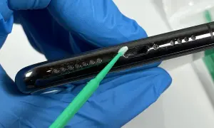 Rękawiczka z niebieskiej gumy delikatnie czyści telefon z kurzu za pomocą zielonego patyczka.