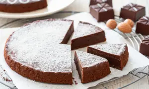 Una torta tenerina al cioccolato, spolverata di zucchero a velo, con fette tagliate e praline di cioccolato intorno.