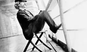 Mark Twain sitter på en stol på ett skeppsdäck, med en hatt och en mustasch. En bild som inspirerar till ett mark twain citat om livet.