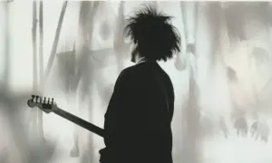 Chłopcy nie płaczą. Robert Smith z The Cure z gitarą, w cieniu, z charakterystyczną fryzurą.