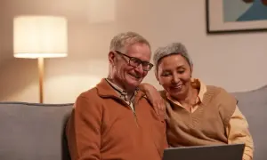 Uśmiechnięta para seniorów przegląda coś na laptopie. Może planują urlop bezpłatny, by cieszyć się emeryturą.