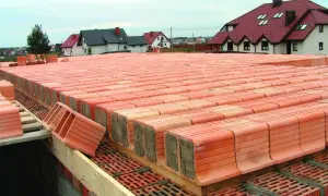 Strop ackermana w budowie, rzędy pustaków ceramicznych czekają na betonowanie. W tle domy z czerwonymi dachami.