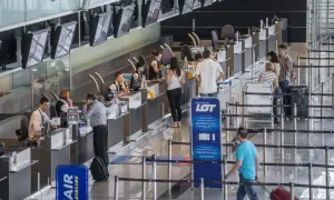 Kolejka do odprawy na lotnisku. Ludzie czekają na boarding, pracownicy obsługują stanowiska.