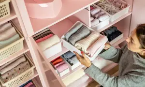 Donna sistema maglioni e calzini in contenitori per organizzare spazi casa. Armadio rosa ordinato con vestiti piegati.