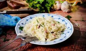 Herzhaftes Krautsalat Rezept mit Speck und frischen Kräutern, serviert auf einem blauen Tellerchen. Dazu Brot, Knoblauch und Petersilie.