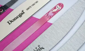 Różne pilniki do paznokci, w tym szklany z kotkiem i sercem, oraz papierowe o różnej gradacji pilnika.