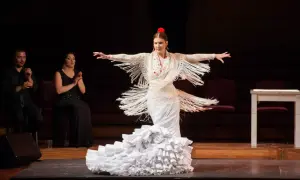 Bailarina de flamenco con vestido blanco y volantes, expresando pasión. A su lado, dos personas aplauden.
