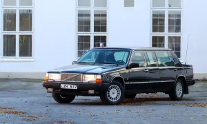 Svart, förlängd 760 Volvo med blåljus på taket, parkerad framför en vit byggnad med stora fönster.