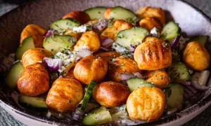 Knuspriger Gnocchi Salat mit Gurken, roten Zwiebeln und einem cremigen Dressing, garniert mit Kräutern.