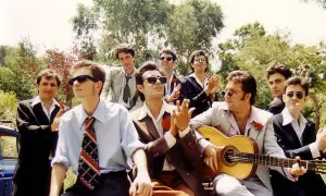 Grupo de hombres con trajes, uno toca la guitarra, listos para una rumba catalana bajo el sol.