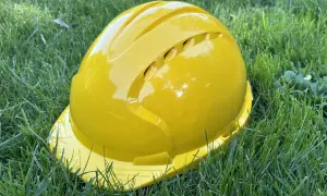 Żółty kask ochronny leży na trawie. Pamiętaj o sprawdzeniu **daty ważności kasku ochronnego** przed użyciem.