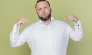 Mann zeigt auf sich und sein weißes Hemd. Er fragt sich, welches Unterhemd unter dem Hemd am besten passt.