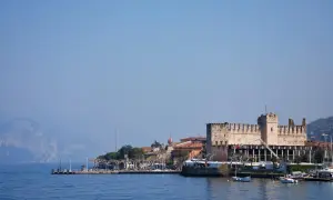 Rocchetta di Moniga del Garda, un gioiello da vedere sul lago. Passeggiata sul lungolago con barche e montagne sullo sfondo.